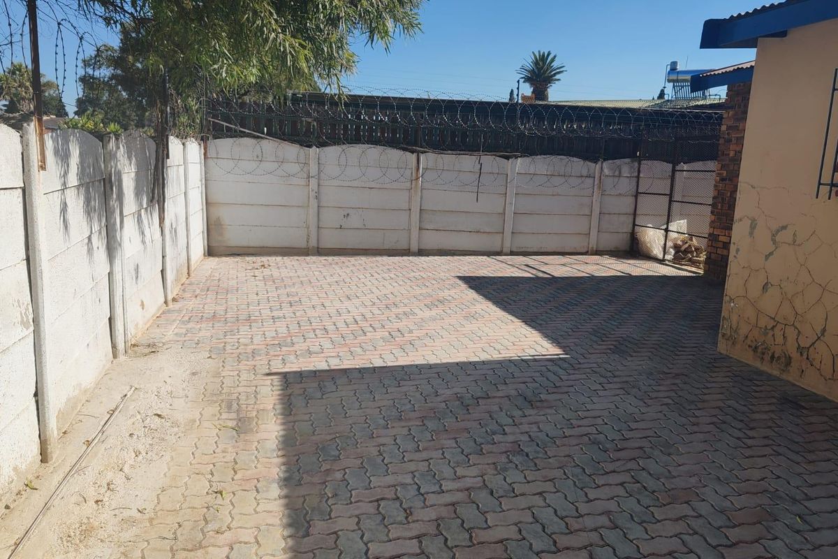 A paved rear courtyard area enclosed by precast concrete walls topped with razor wire security fencing.