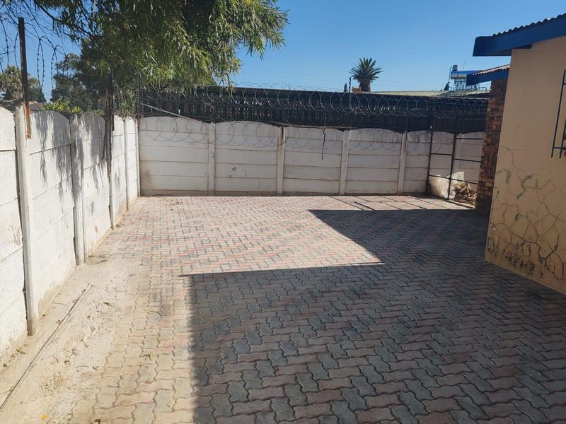 A paved rear courtyard area enclosed by precast concrete walls topped with razor wire security fencing.