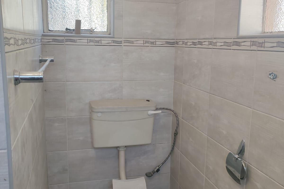 A compact bathroom featuring tiled walls and flooring, equipped with a standard toilet and obscured glass windows for privacy.