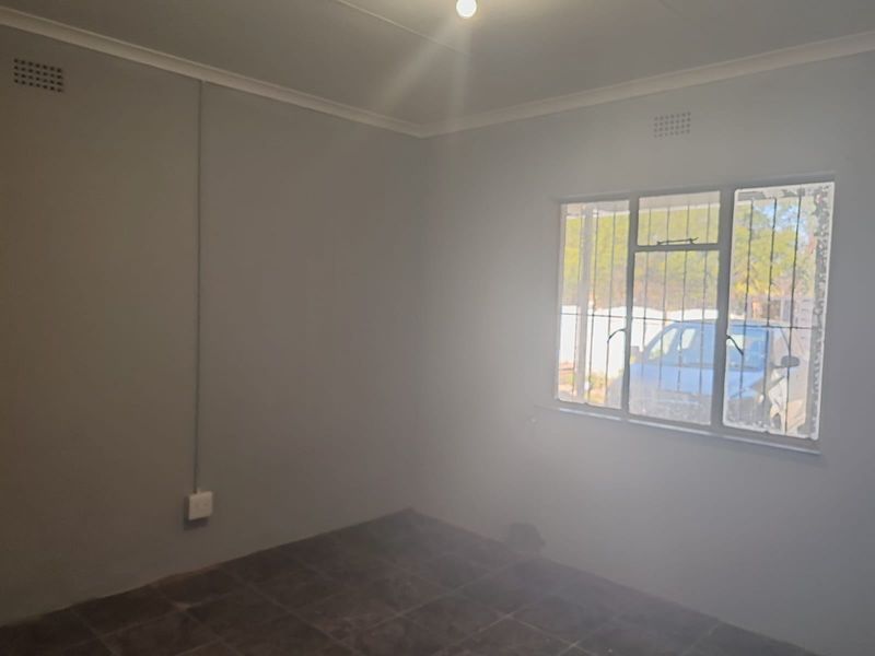 An empty bedroom featuring tiled flooring, security bars on the window, and visible surface-mounted electrical conduit.