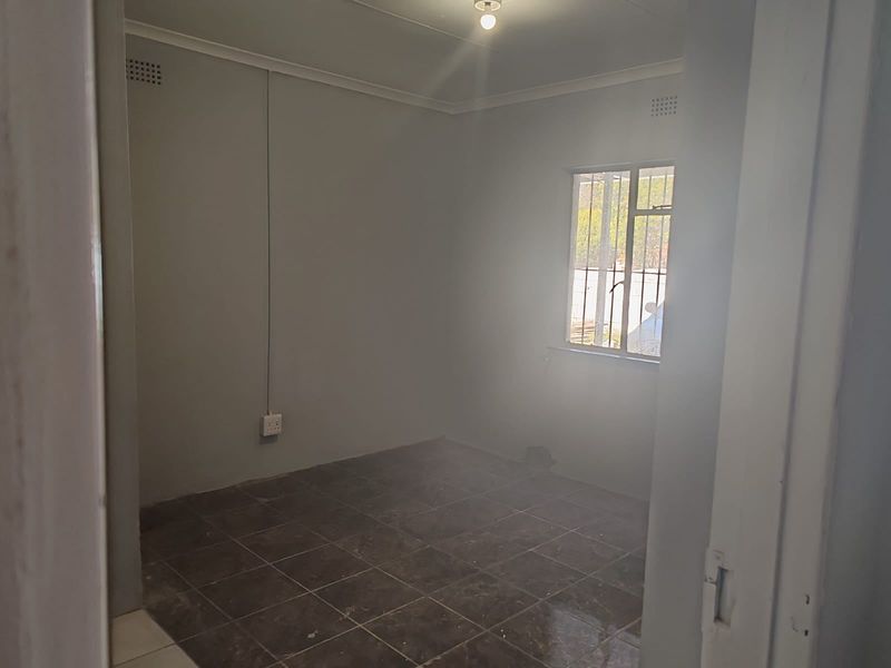An empty bedroom featuring tiled flooring, security bars on the window, and neutral wall finishes, ready for personalization.