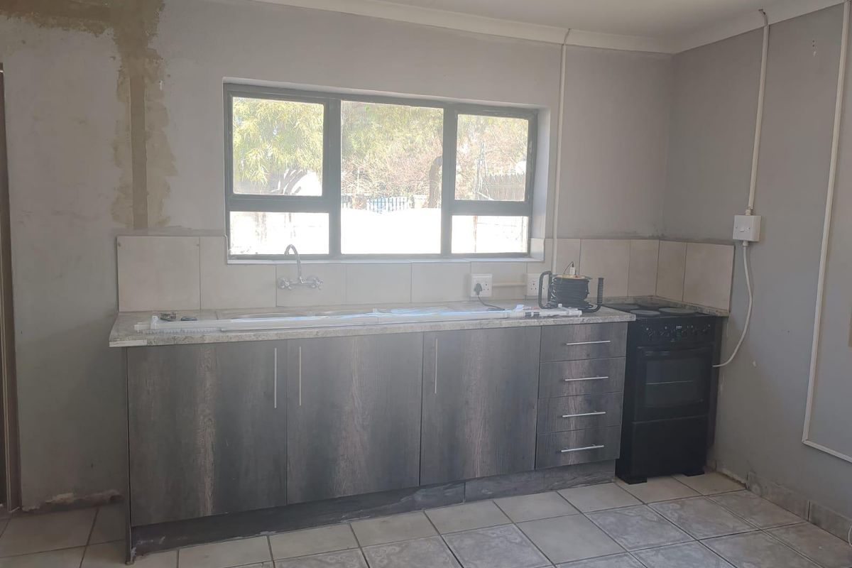 A functional kitchen space featuring dark wood-finish cabinetry, tiled flooring, and a freestanding stove, currently requiring final wall finishing and cosmetic updates.