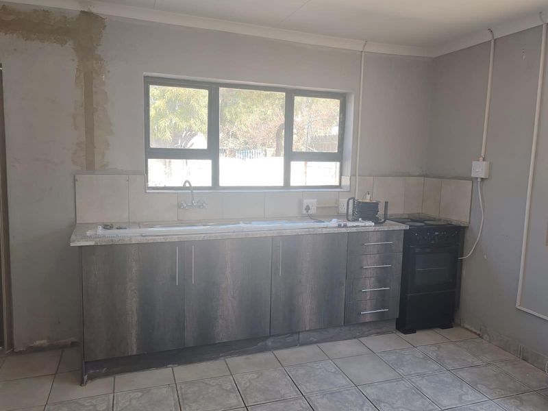 A functional kitchen space featuring dark wood-finish cabinetry, tiled flooring, and a freestanding stove, currently requiring final wall finishing and cosmetic updates.