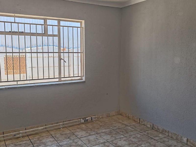 An empty bedroom featuring tiled flooring, neutral grey walls, and a window fitted with security bars.