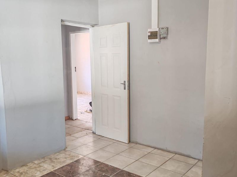An empty hallway featuring tiled flooring, a prepaid electricity meter, and access to an adjoining room through a white internal door.