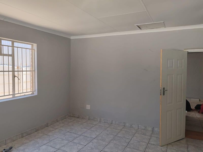 An empty bedroom featuring tiled flooring, security bars on the window, and neutral wall finishes, providing a blank canvas for personalization.