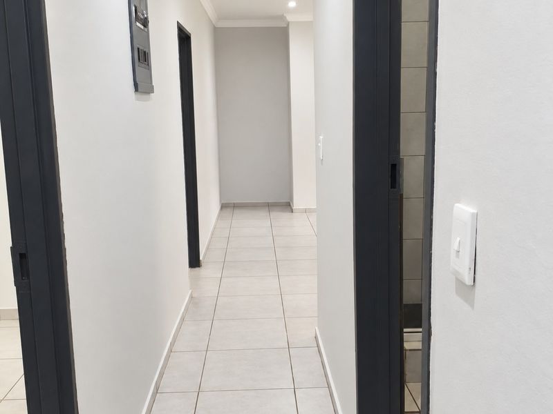 A clean, modern hallway featuring neutral tiled flooring, recessed downlighting, and dark-framed doorways leading to adjacent rooms.