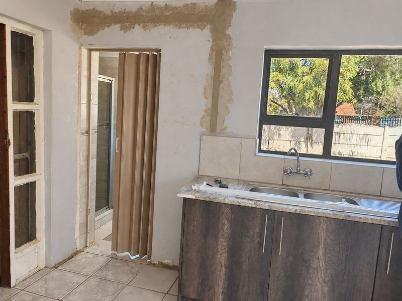 A kitchen area featuring a double sink, laminate countertops, and base cabinetry, currently undergoing renovation with unfinished wall surfaces.