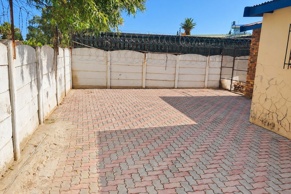 A paved rear courtyard area enclosed by precast concrete walls with security razor wire, featuring visible exterior wall plaster damage.