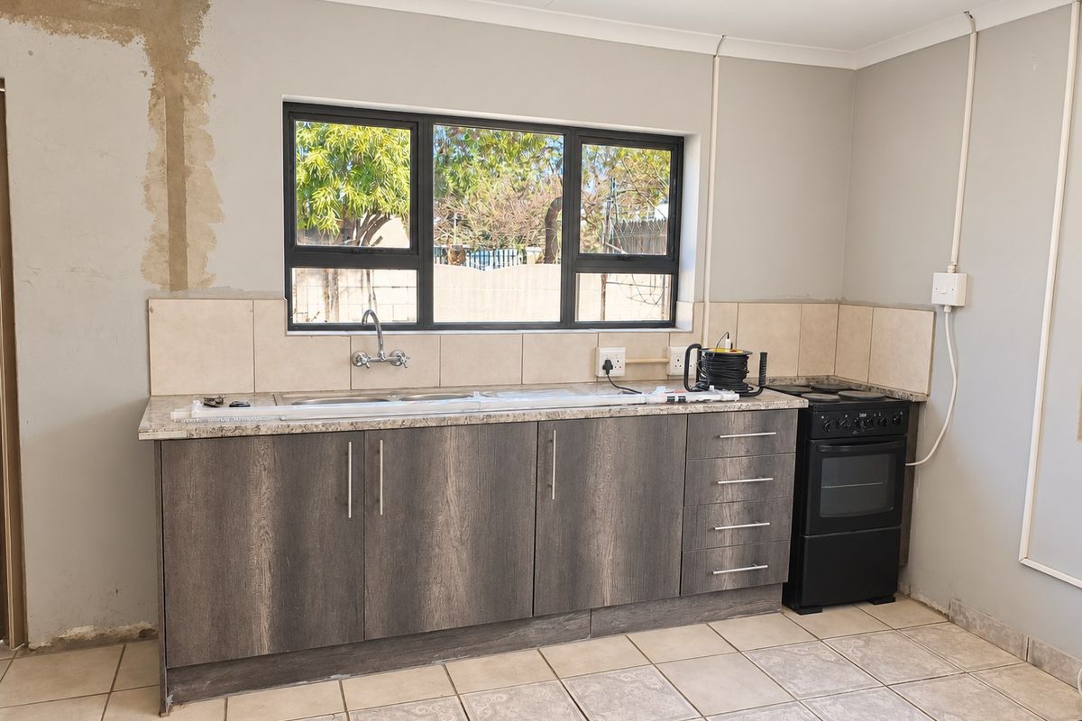 A functional kitchen featuring dark wood-grain cabinetry, granite countertops, and a tiled backsplash, currently requiring minor finishing work to the walls and electrical installations.