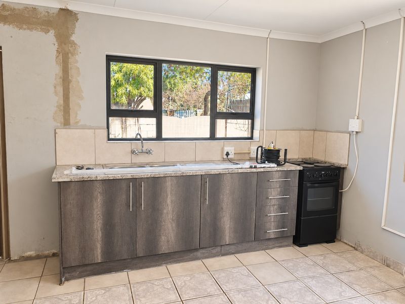 A functional kitchen featuring dark wood-grain cabinetry, granite countertops, and a tiled backsplash, currently requiring minor finishing work to the walls and electrical installations.