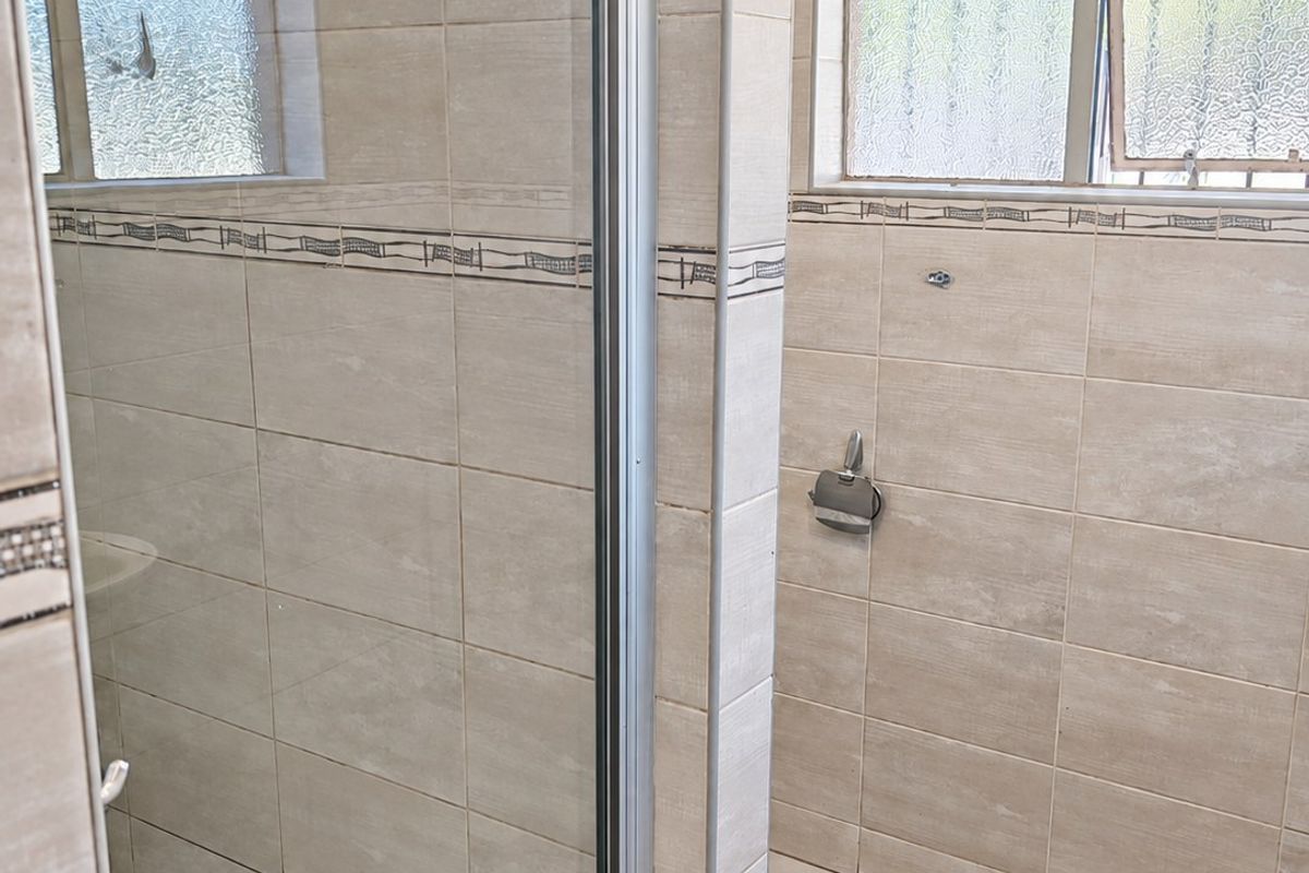 A functional bathroom space featuring a tiled shower enclosure with a glass door and neutral wall tiling, currently awaiting new fixtures.