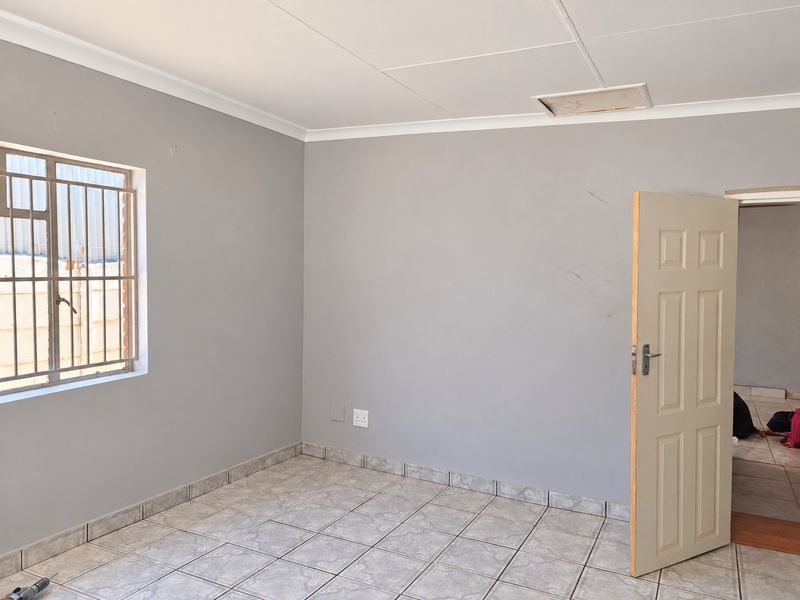 An empty bedroom featuring tiled flooring, security bars on the window, and a ceiling access hatch, presenting a clean canvas for personalization.