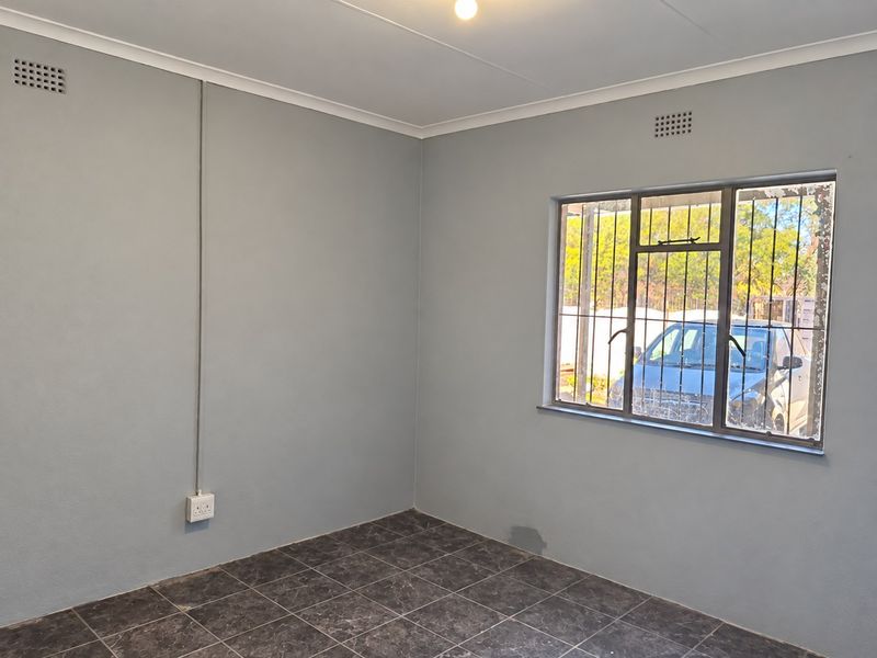 An empty bedroom featuring tiled flooring, security bars on the window, and neutral grey walls with visible maintenance requirements.