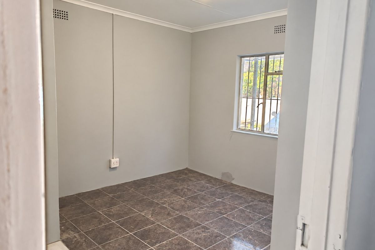A vacant bedroom featuring tiled flooring, security bars on the window, and neutral wall finishes, ready for personalization.
