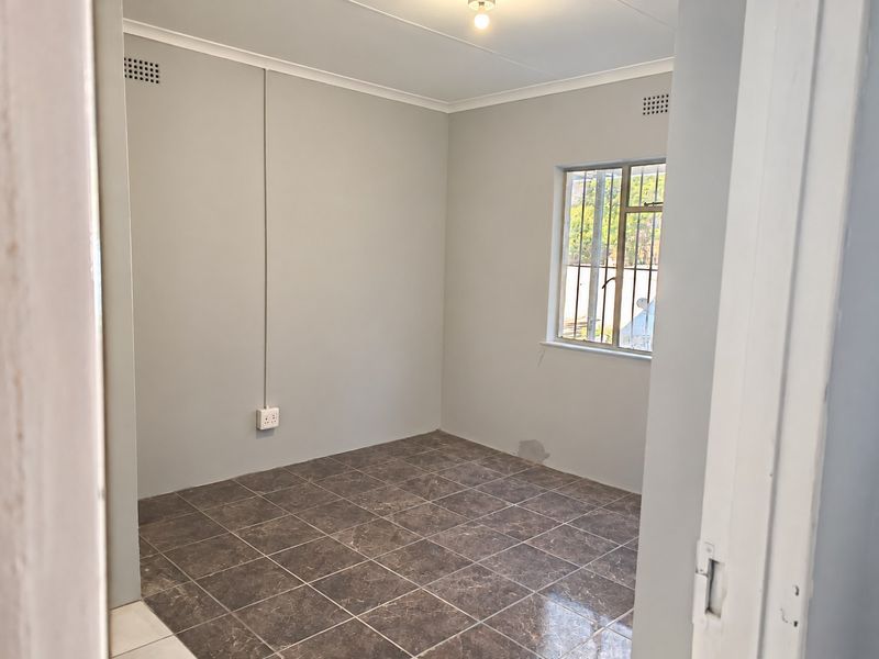 A vacant bedroom featuring tiled flooring, security bars on the window, and neutral wall finishes, ready for personalization.
