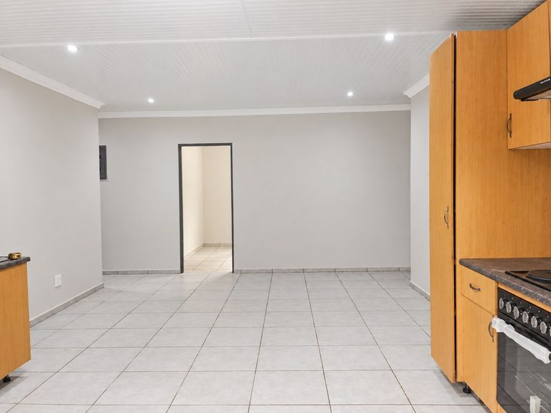 An empty, well-lit kitchen featuring light wood cabinetry, a built-in oven and hob, and neutral tiled flooring throughout.