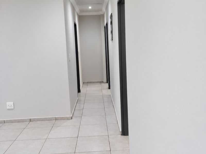 A clean, modern hallway featuring neutral ceramic floor tiles, recessed downlighting, and decorative ceiling cornicing, providing a bright and well-maintained transition space.