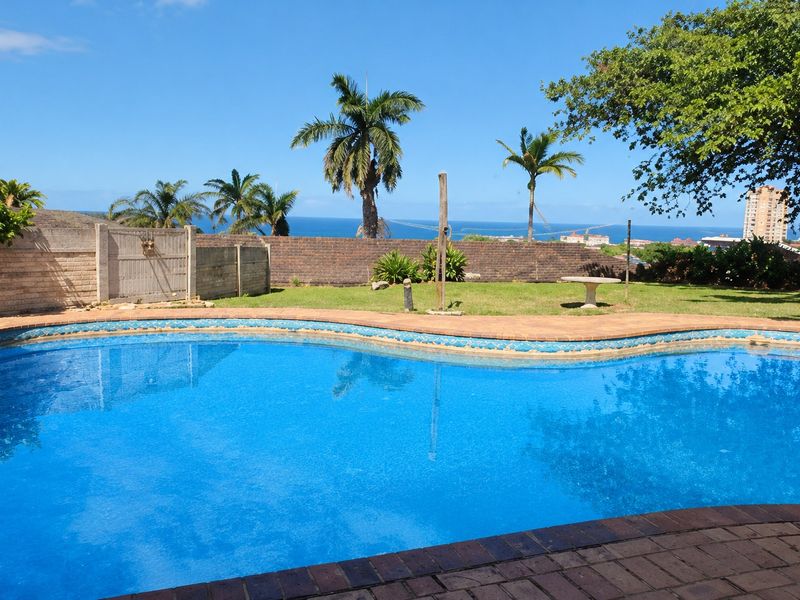 Outdoor pool area featuring a swimming pool with paved coping, a lawn, and a brick boundary wall with scenic ocean views.