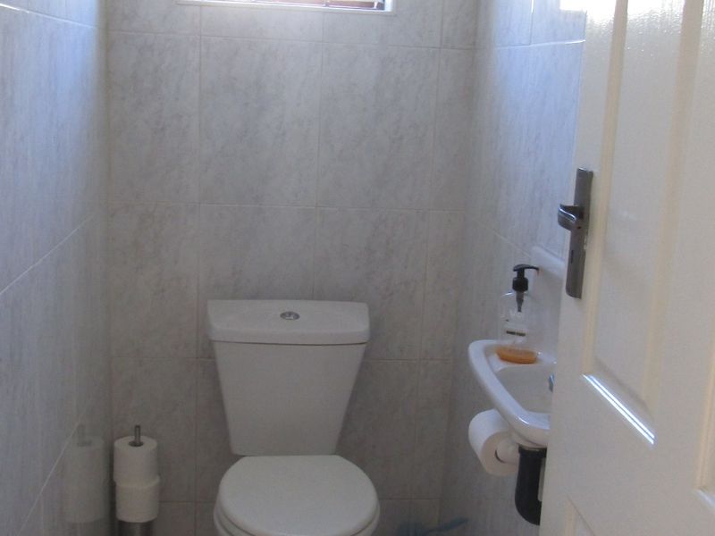 A compact guest bathroom featuring a white toilet, wall-mounted basin, and neutral floor-to-ceiling tiling.