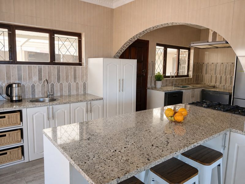 A well-appointed kitchen featuring granite countertops, white cabinetry, a gas hob with extractor fan, and a decorative archway connecting to the adjacent space.