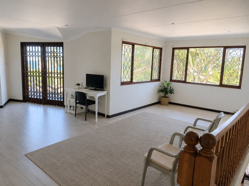 Spacious living area featuring light laminate flooring, timber-framed windows, and a secure trellis gate leading to an outdoor space.