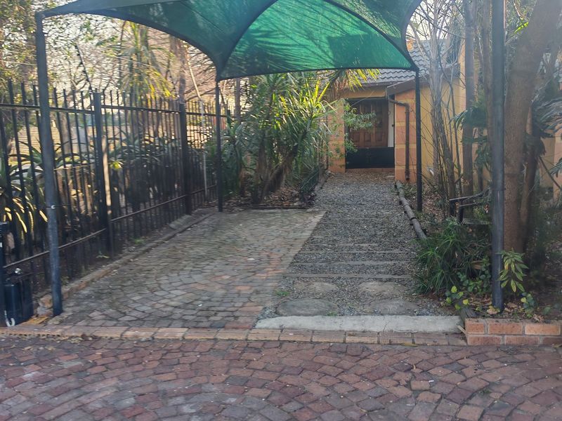 Front exterior view featuring a shaded parking area, paved driveway, and gravel pathway leading to the main entrance.