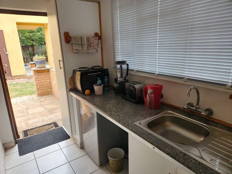 A functional scullery area featuring a stainless steel sink, laminate countertop, and direct access to an outdoor patio space.