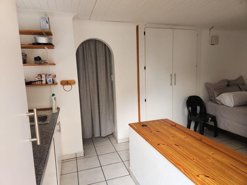 Compact open-plan studio space featuring a kitchenette with stone countertops, a timber breakfast bar, tiled flooring, and a built-in wardrobe.