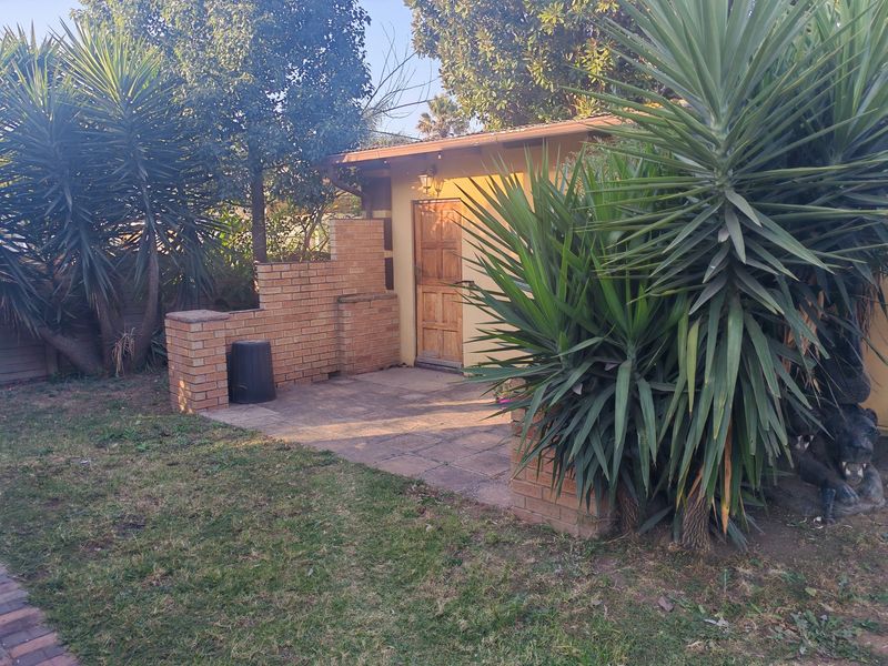 A rear exterior view featuring a paved patio area, a brick privacy wall, and a wooden entrance door set within a landscaped garden.