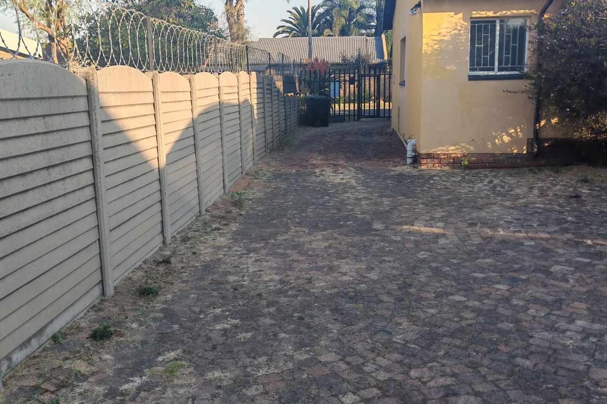 Rear exterior view showing a paved driveway, precast concrete boundary wall with razor wire, and the side elevation of the house.