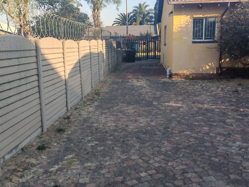 Rear exterior view showing a paved driveway, precast concrete boundary wall with razor wire, and the side elevation of the house.