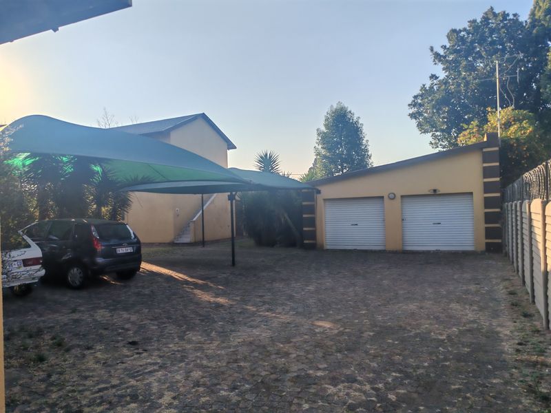 Exterior view of a double garage with roll-up doors, a paved driveway, and a shade cloth carport structure.