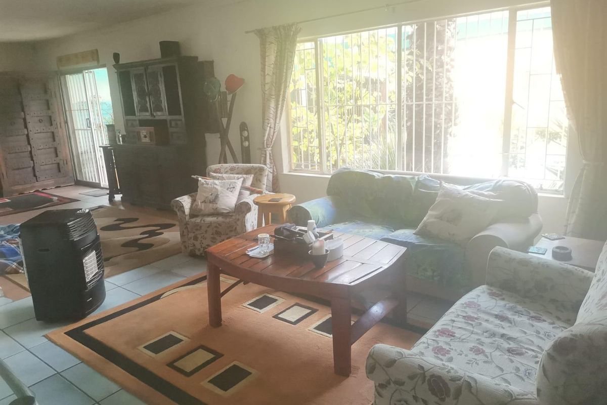 A spacious living room featuring tiled flooring, large windows with security bars, and a sliding glass door providing access to the exterior.