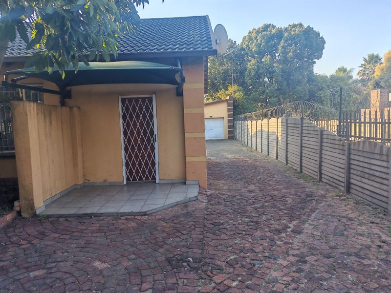 Front exterior view showing a paved driveway, security gate, covered entrance area, and a detached garage with perimeter walling.