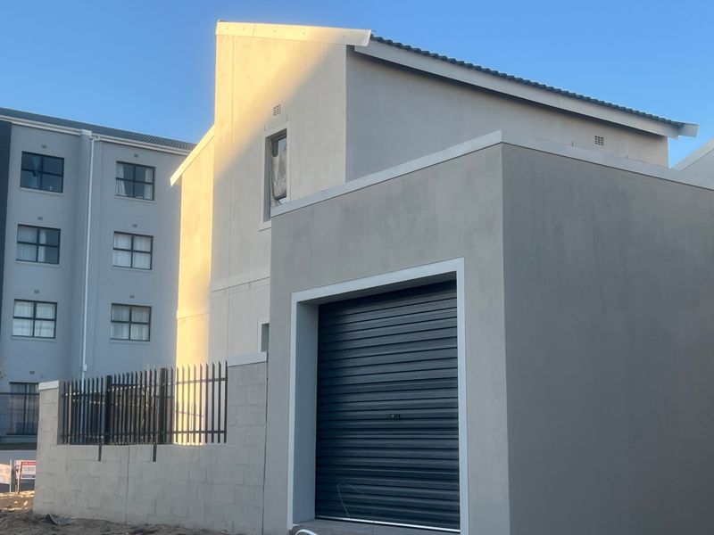 A modern residential exterior featuring a clean plastered facade, a secure roller garage door, and metal perimeter fencing.