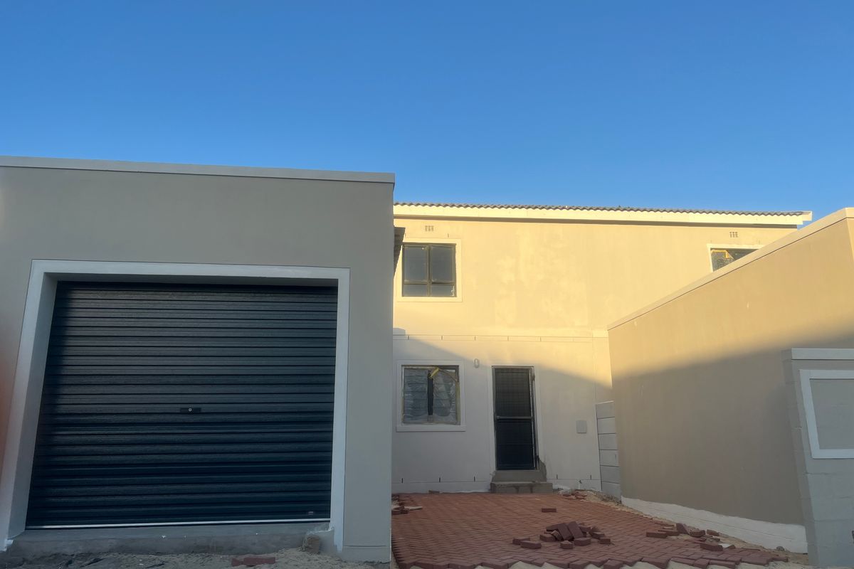 Rear view of a modern two-story house featuring a roller garage door, paved patio area, and neutral exterior wall finishes.