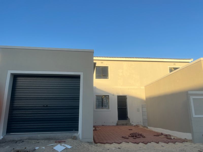 Rear view of a modern two-story house featuring a roller garage door, paved patio area, and neutral exterior wall finishes.