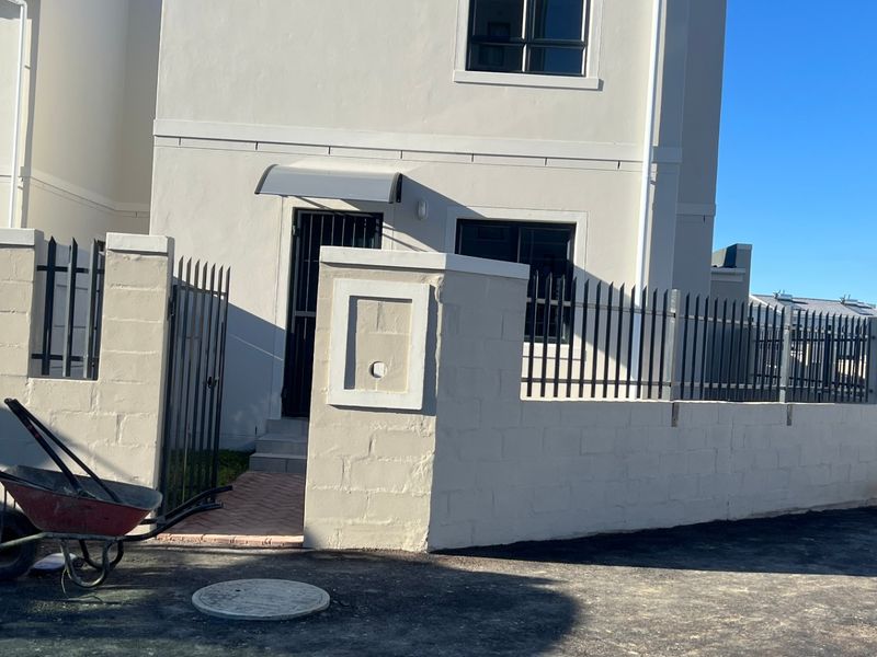 Front elevation of a modern two-story house featuring a perimeter wall, metal security fencing, and a solar water heating system on the roof.