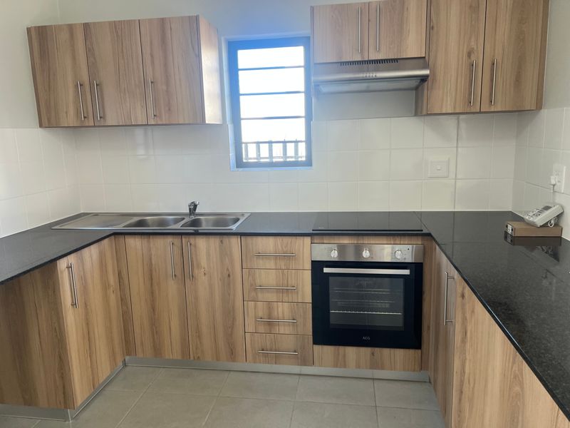 A clean, modern kitchen featuring wood-look cabinetry, granite countertops, built-in oven, electric hob, and a tiled backsplash.