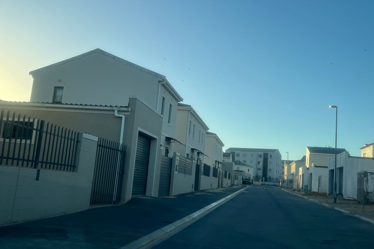 A street view of a modern residential estate featuring paved roads, street lighting, and contemporary houses with boundary walls and garage access.