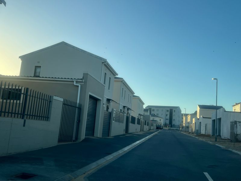 A street view of a modern residential estate featuring paved roads, street lighting, and contemporary houses with boundary walls and garage access.