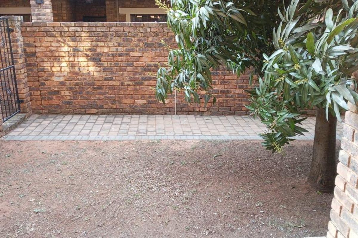 A private rear courtyard featuring a face brick boundary wall, paved patio section, and established tree, offering potential for landscaping improvements.