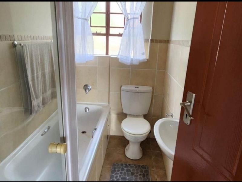 A functional bathroom featuring a bathtub, pedestal basin, and toilet with neutral wall and floor tiling.