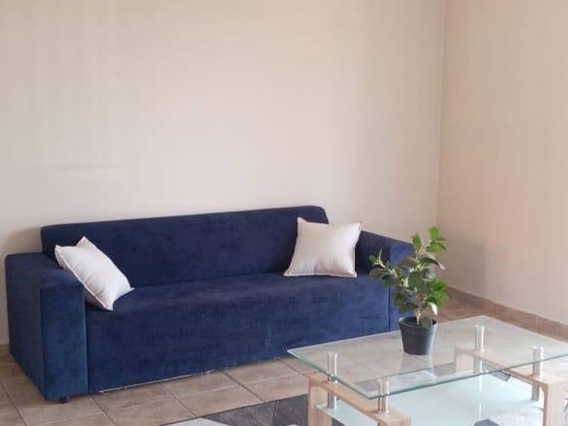 A simple living room area featuring neutral wall tones, tiled flooring, and a ceiling-mounted light fixture.