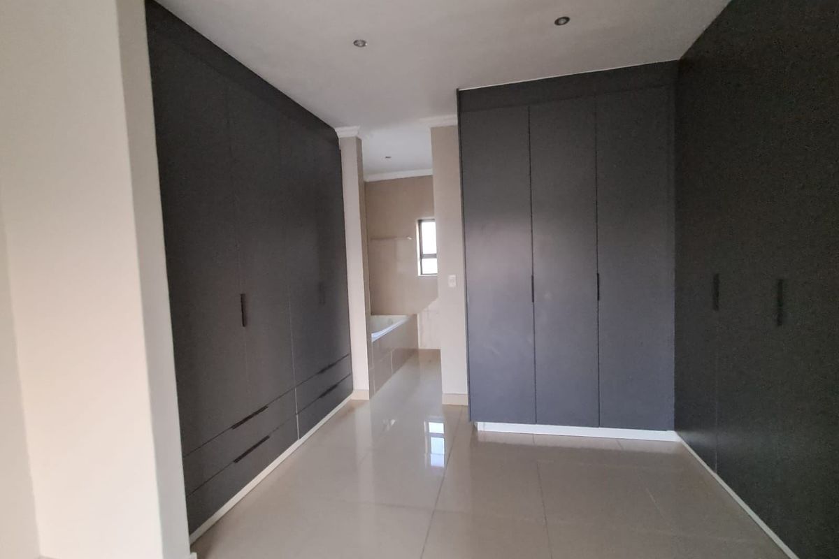 Spacious bedroom featuring extensive dark grey built-in cupboards, polished tiled flooring, and direct access to an en-suite bathroom.
