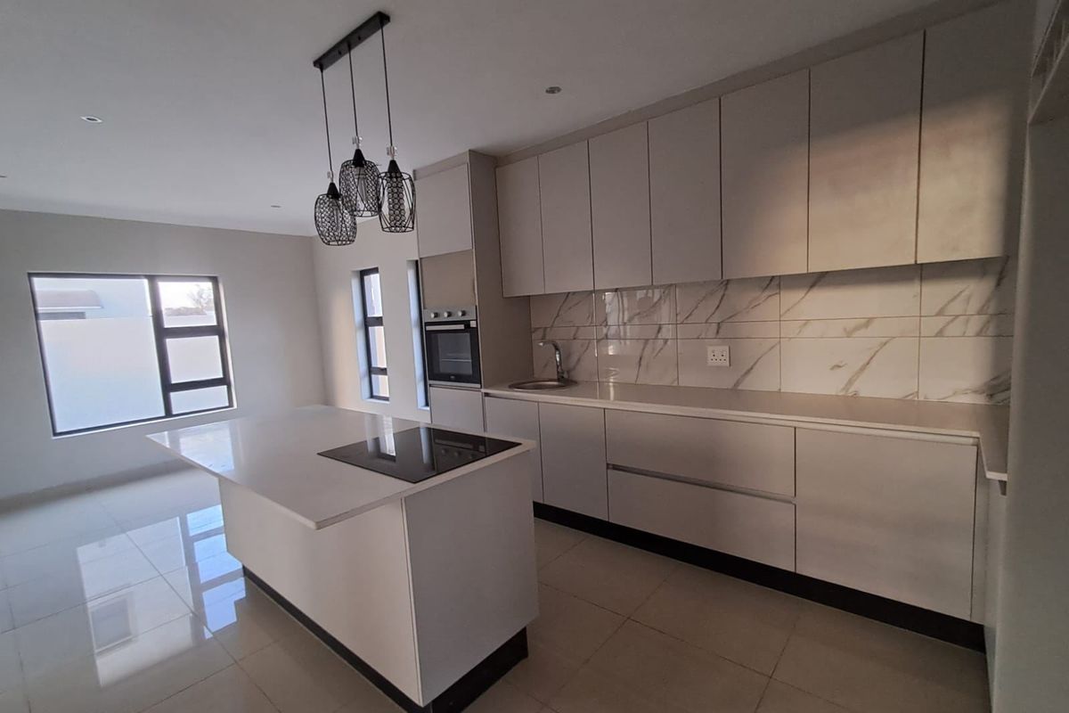 Modern kitchen featuring sleek white cabinetry, a central island with an integrated hob, stone countertops, and a stylish marble-look tile backsplash.