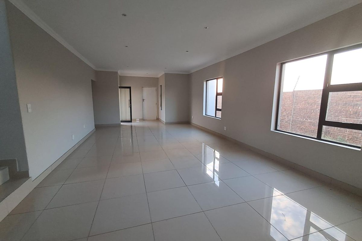 A spacious, empty living area featuring neutral walls, large aluminium windows, and polished tiled flooring with recessed lighting.
