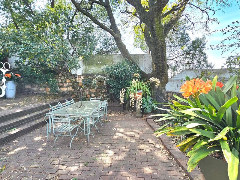 A charming outdoor patio area featuring brick paving, a stone retaining wall, and mature trees, providing a shaded space for outdoor dining.