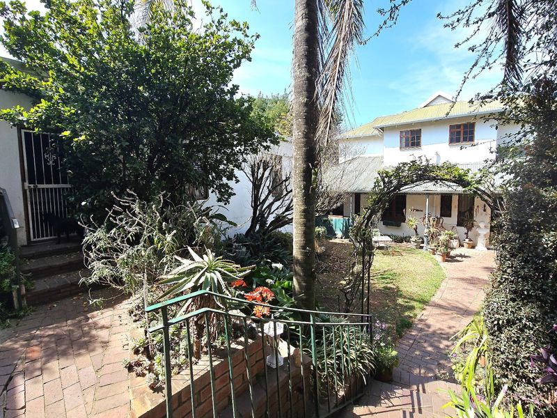 A rear garden area featuring a brick paved pathway, established landscaping, and access to the main house structure.